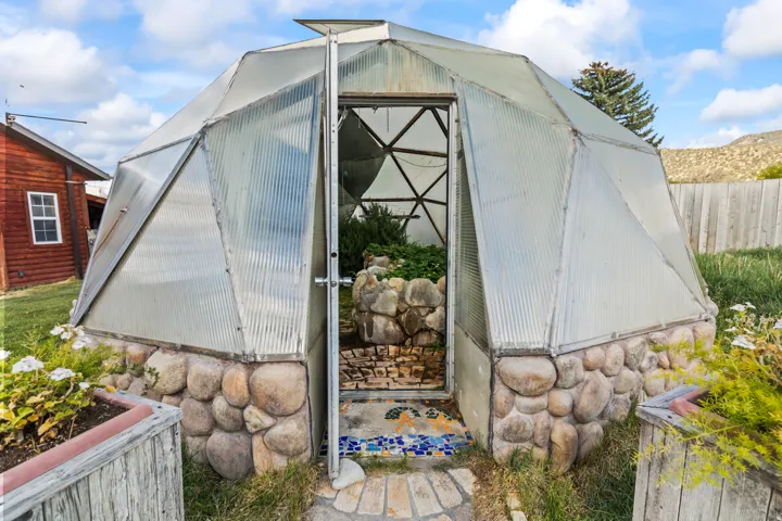 Geodesic dome greenhouse featuring a stone base and translucent panel construction
