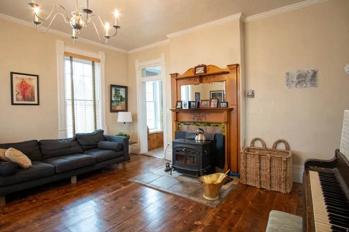 Living room with dark wood finished floors, ornamental molding, a wood stove, and a chandelier