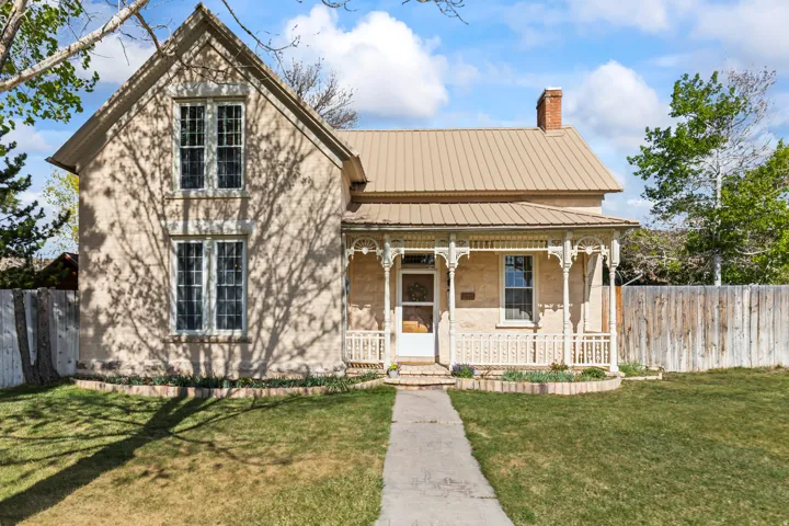 Two-story stucco exterior featuring a metal roof, decorative front porch, brick chimney, and a stone-edged flower bed