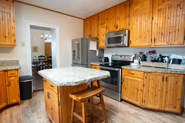 Kitchen featuring stainless steel appliances, light wood-type flooring, ornamental molding, a kitchen island, and a breakfast bar area