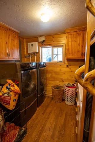 Laundry area featuring cabinet space, wooden walls, wood finished floors, instant hot water heater and  washer and dryer