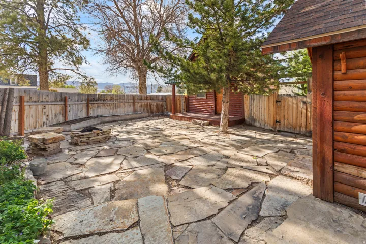 Stone patio featuring a built-in fire pit, privacy fencing, and a separate log-style shed with a shingle roof
