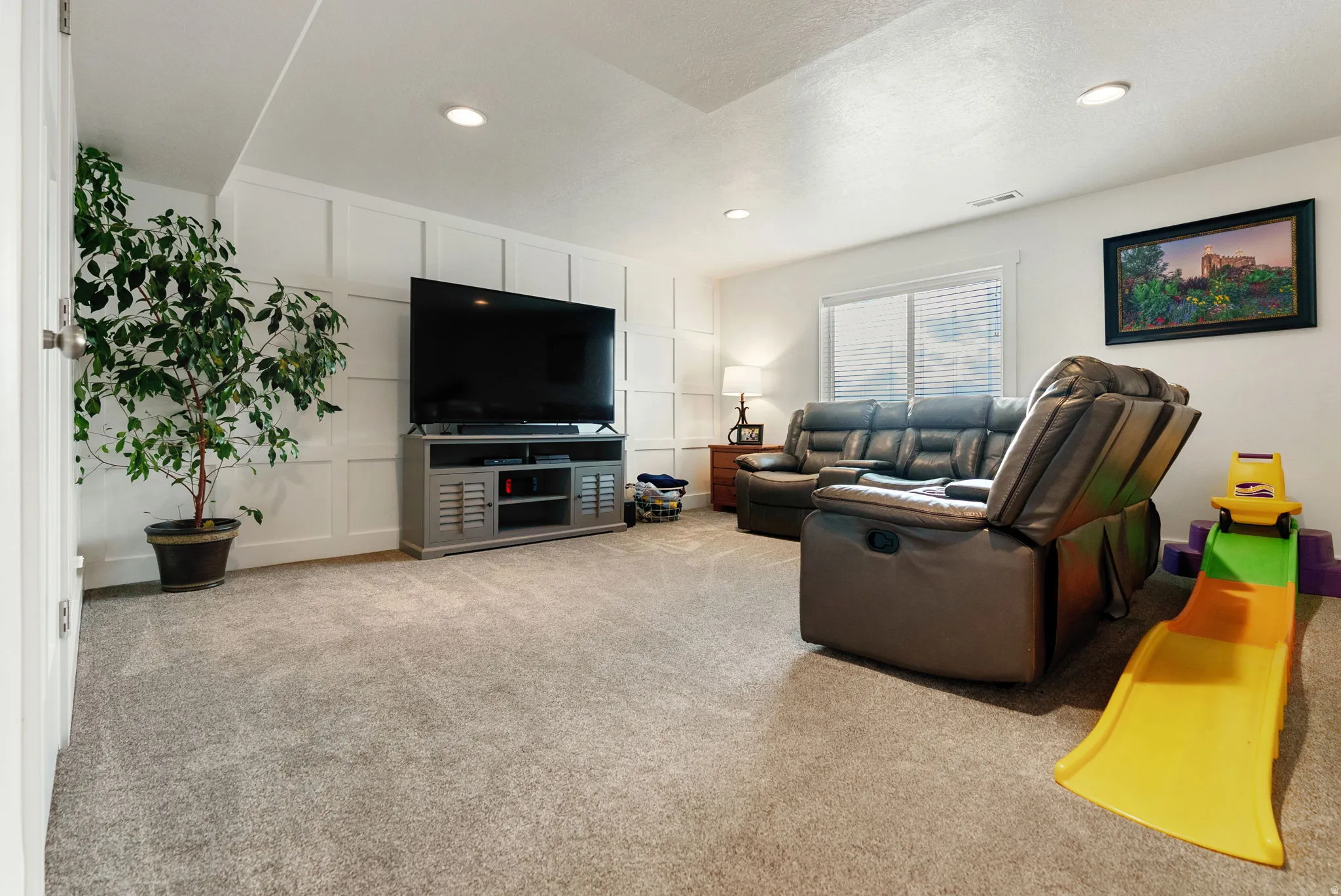 Living area featuring light carpet, recessed lighting, and a decorative wall