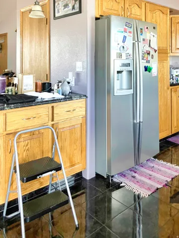 Kitchen with stainless steel fridge, a textured wall, granite tiled floors, and dark stone counters