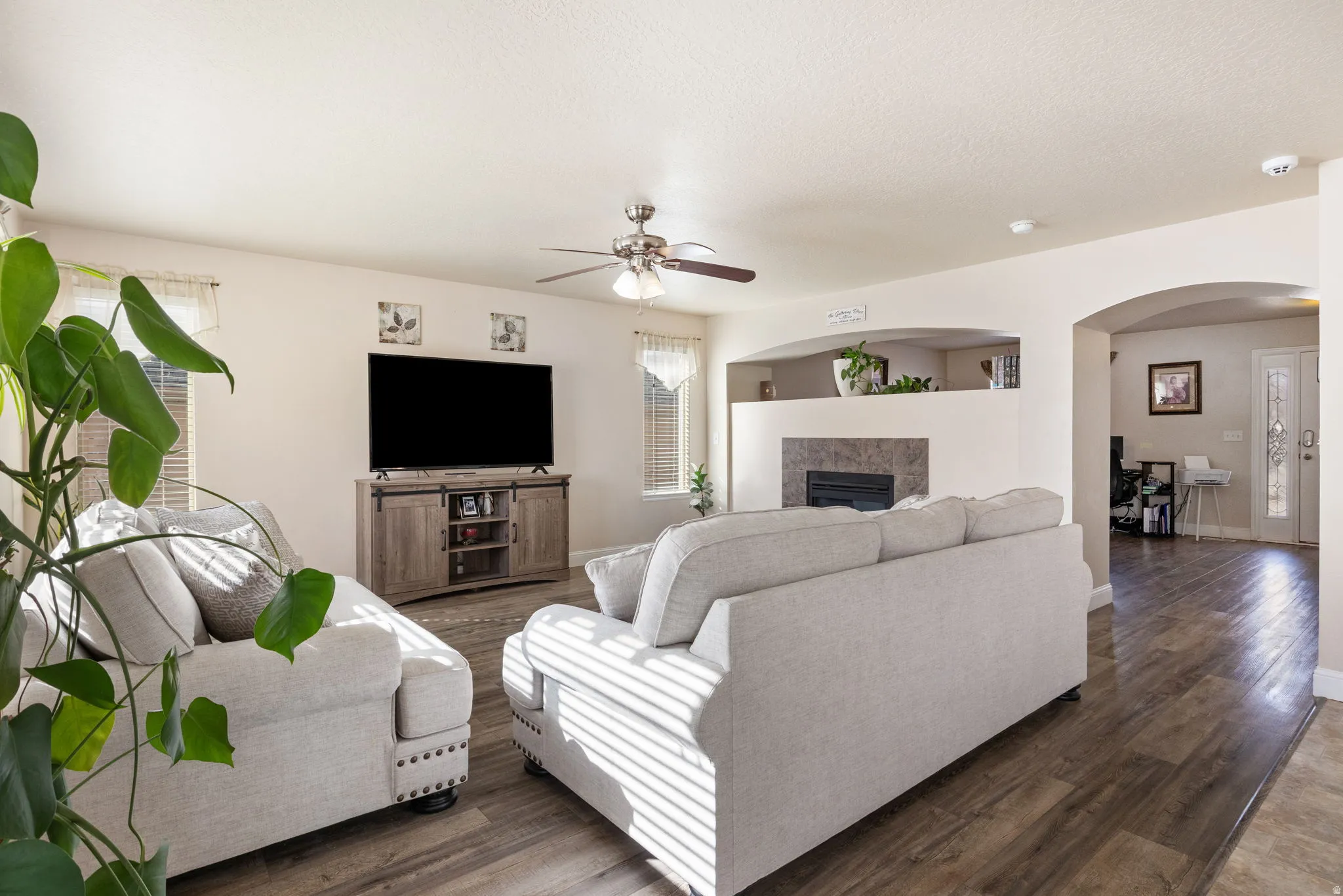 Living room featuring wood finished floors, arched walkways, ceiling fan, and a fireplace