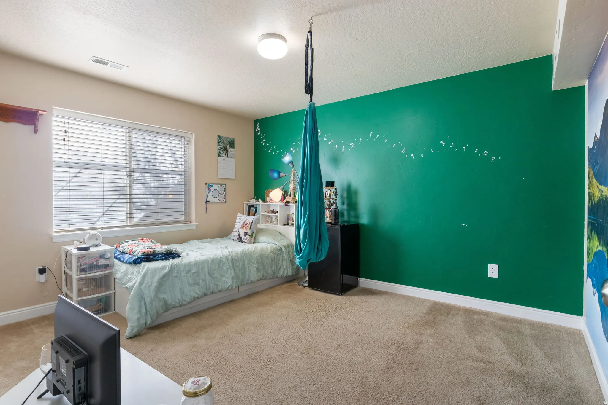 Bedroom featuring light carpet, a textured ceiling, and an accent wall