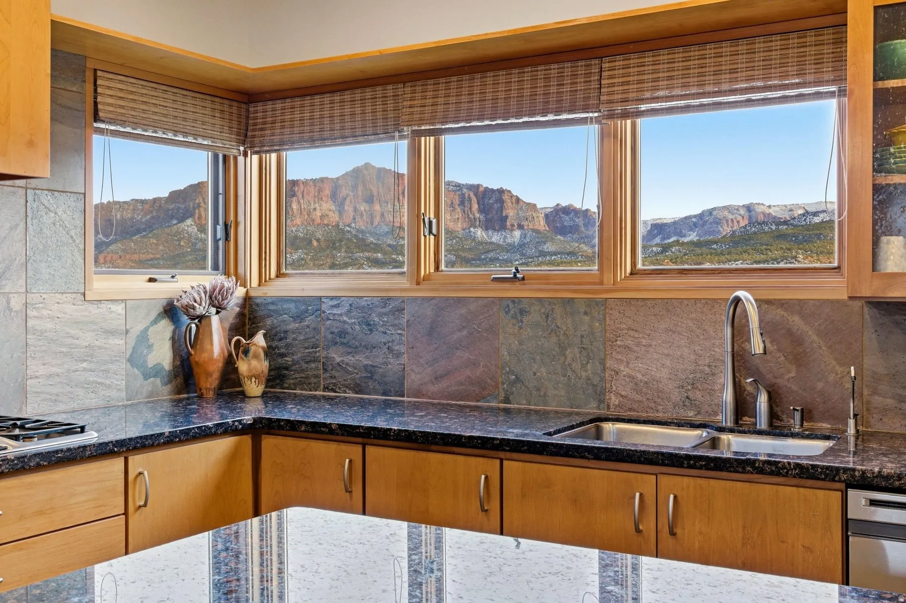 Kitchen view of dark stone counters, wood finish cabinetry, decorative backsplash, and glass fronted cabinets