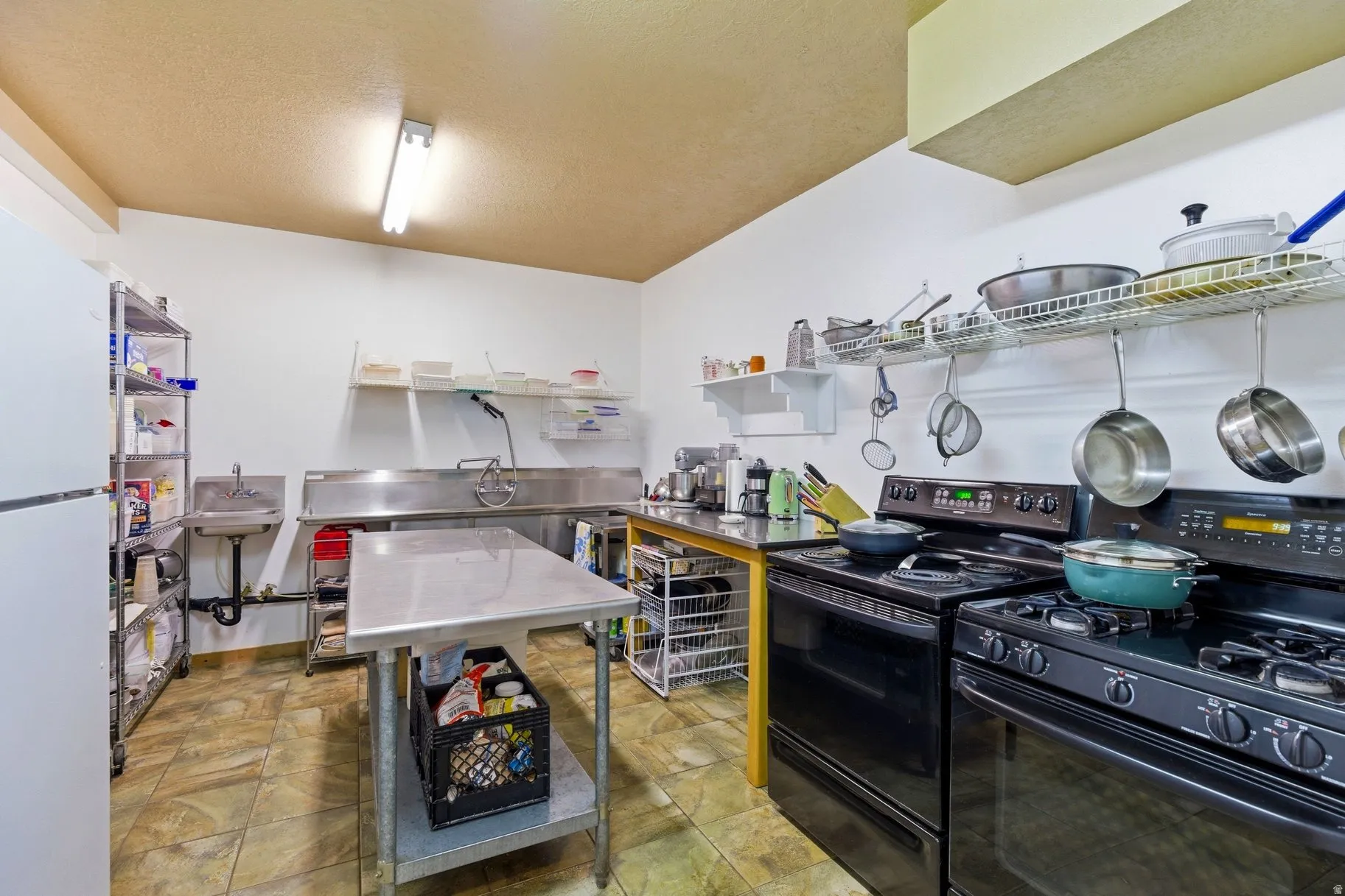 Kitchen with stainless steel countertops, black range with gas cooktop, black range with electric stovetop, freestanding refrigerator, and a textured ceiling