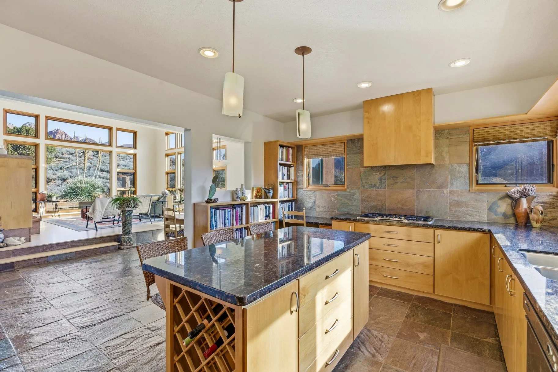 Kitchen with light wood finish cabinets, stone tile floors, and dark stone countertops