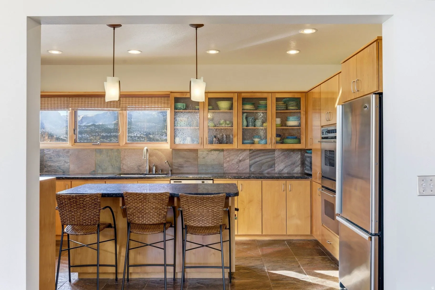 Kitchen featuring stainless steel appliances, pendant lighting, a kitchen breakfast bar, an island with sink, and light wood finish cabinetry
