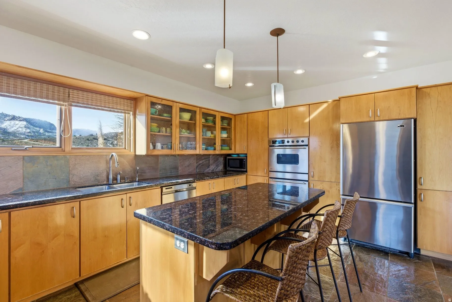 Kitchen featuring stainless steel appliances, a center island, dark stone counters, glass fronted cabinets, and a breakfast bar