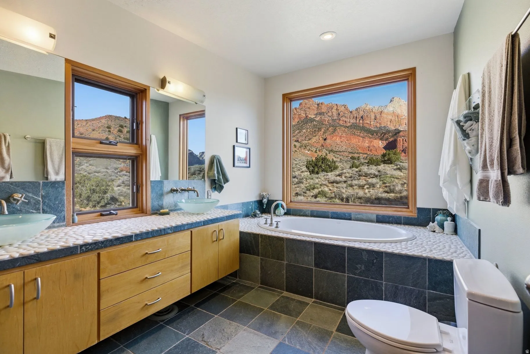 Full bathroom featuring a garden tub, double vanity, and dark stone finish flooring