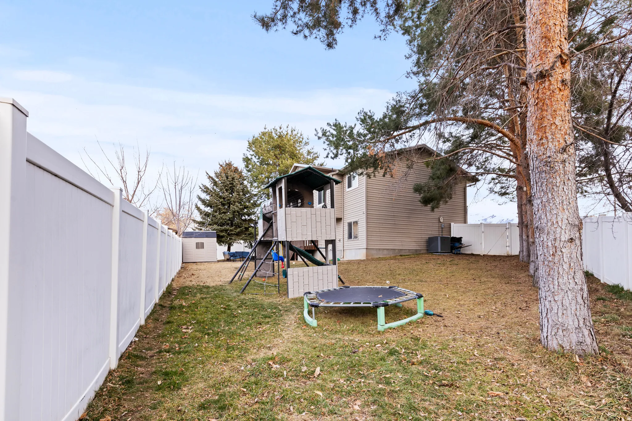Fenced backyard with a playground, a trampoline, and a gate
