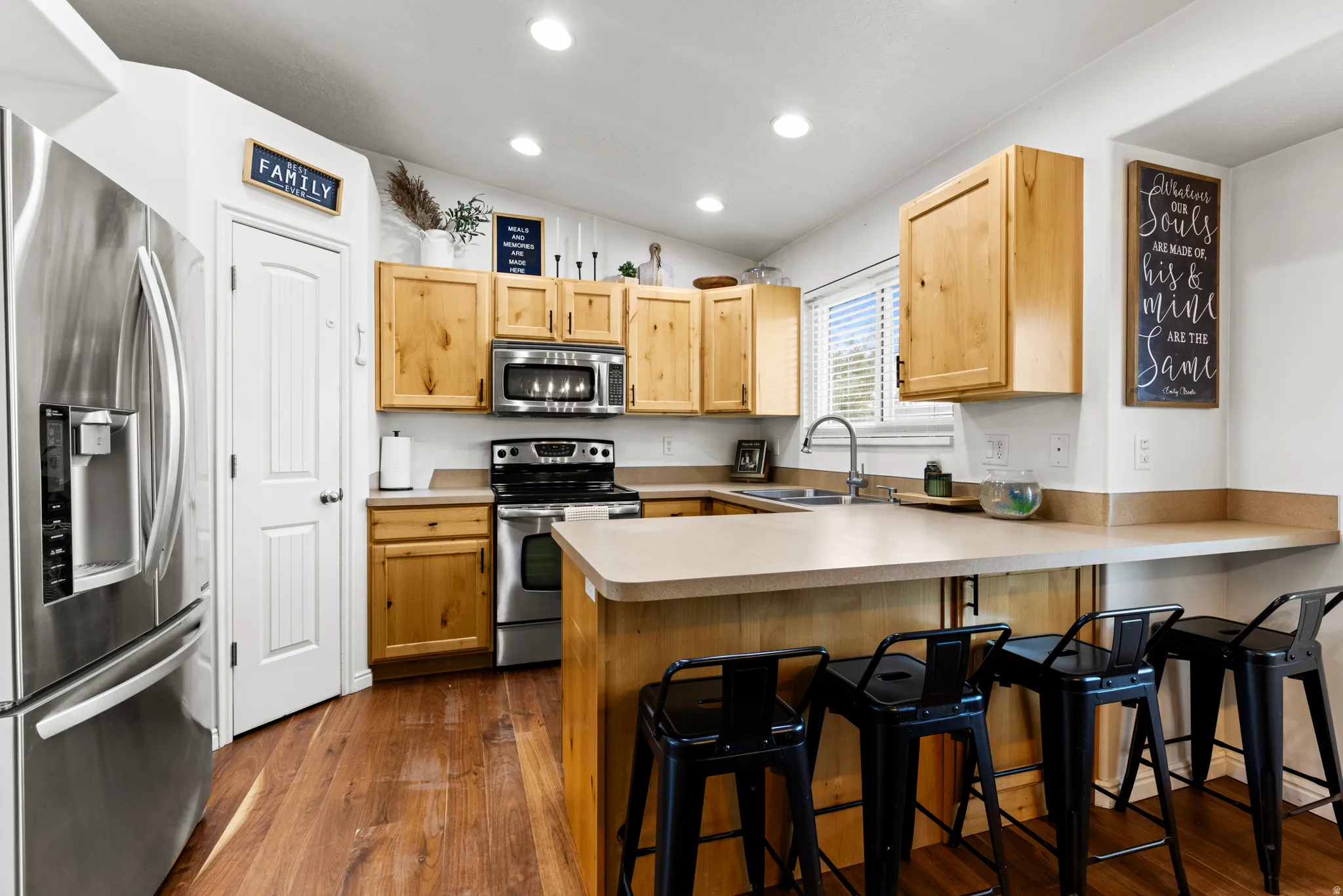 Kitchen featuring stainless steel appliances, a peninsula, a breakfast bar, light countertops, and vaulted ceiling