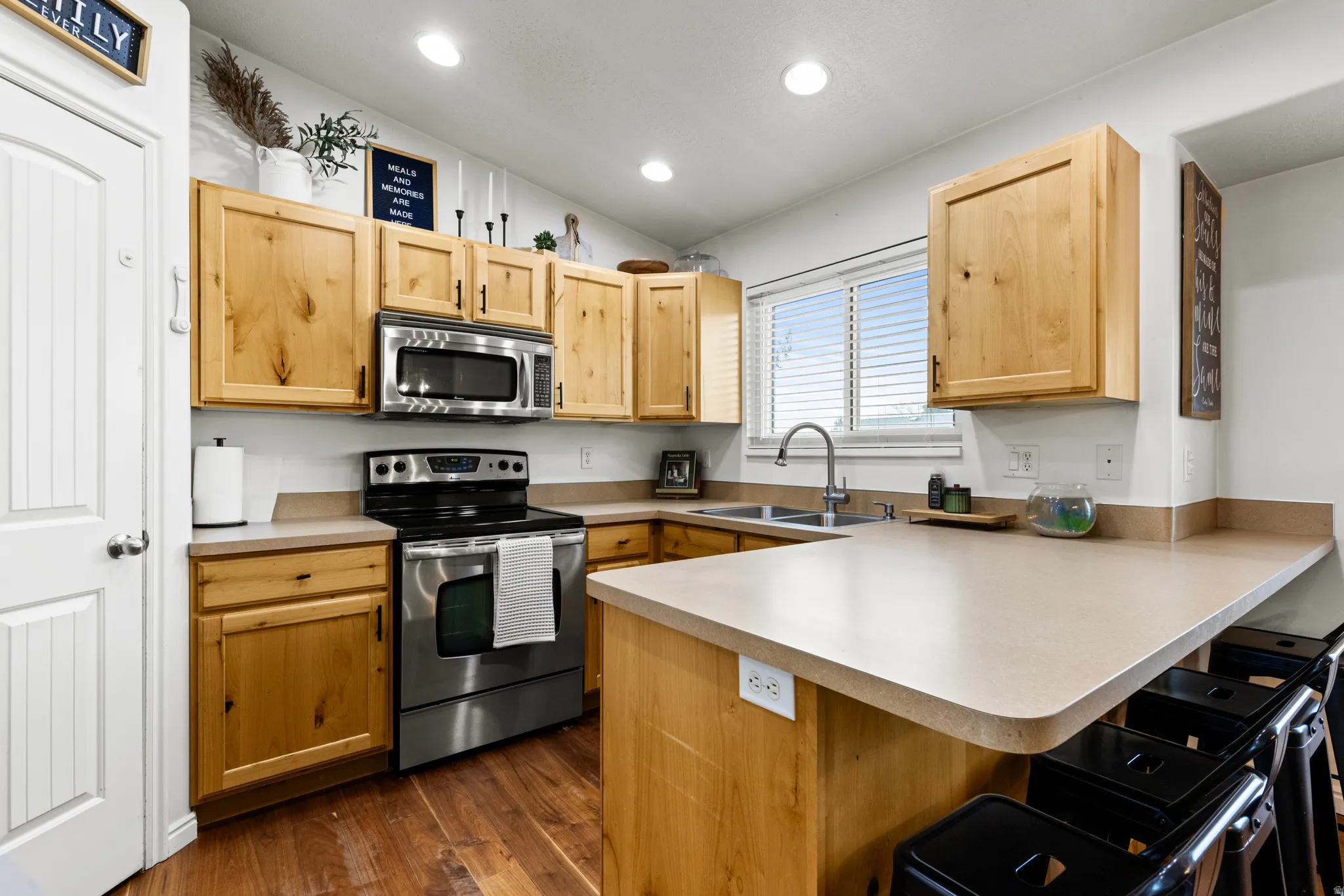 Kitchen with a peninsula, stainless steel appliances, light wood finish cabinets, a kitchen bar, and lofted ceiling