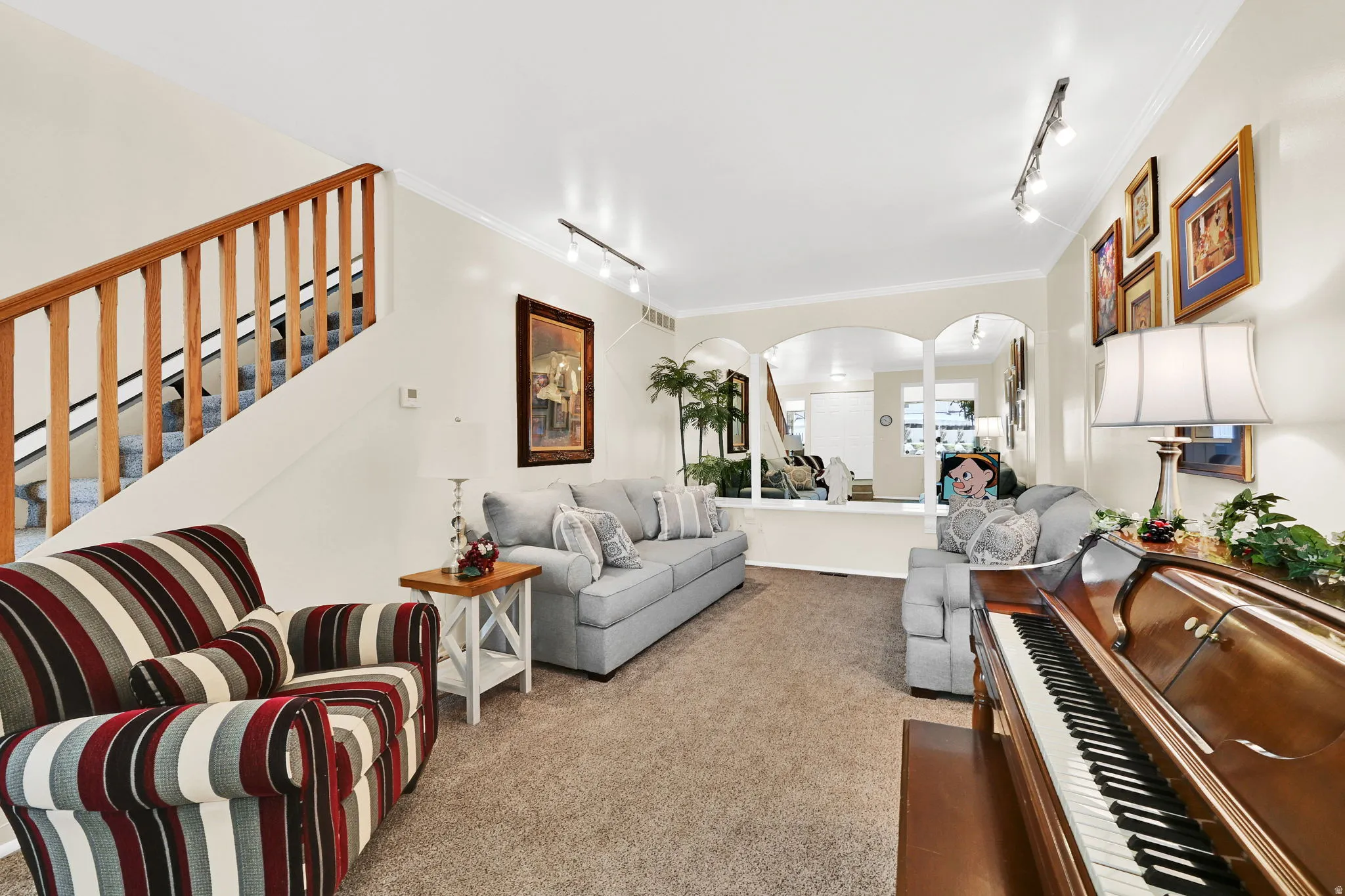 Living area with arched walkways, track lighting, ornamental molding, and light colored carpet