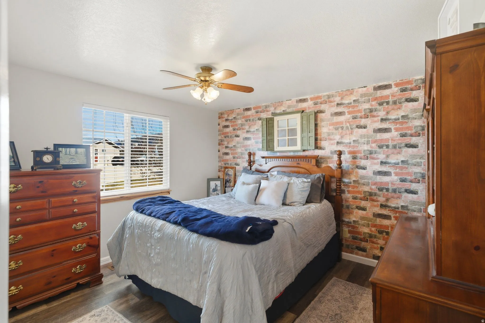 Bedroom with brick wall, dark wood-type flooring, and ceiling fan