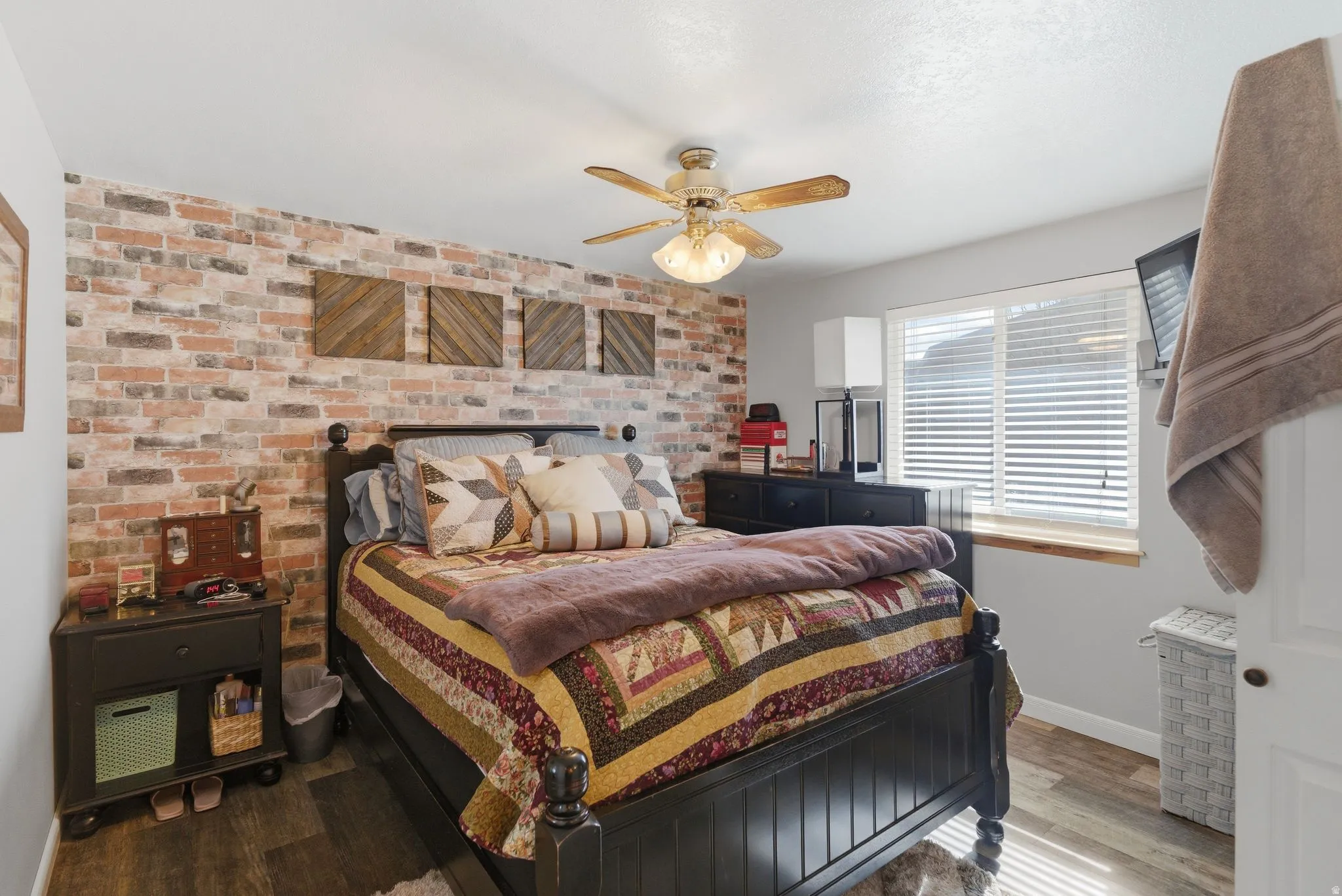 Bedroom with brick wall, wood finished floors, and a ceiling fan