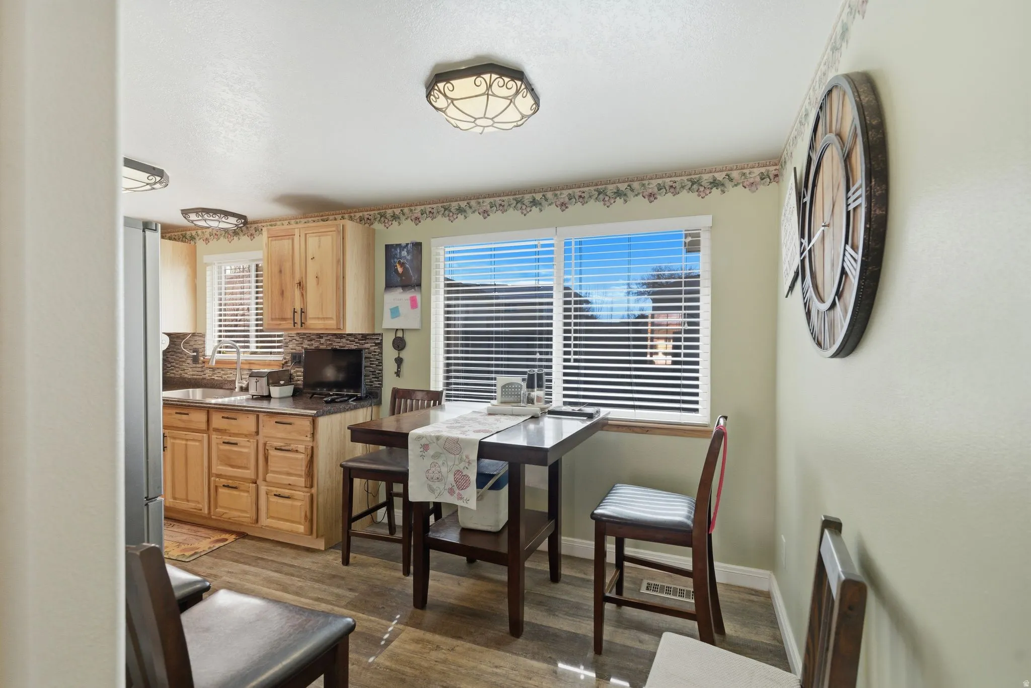 Kitchen with dark wood-style flooring, decorative backsplash, light wood finish cabinetry, and freestanding refrigerator