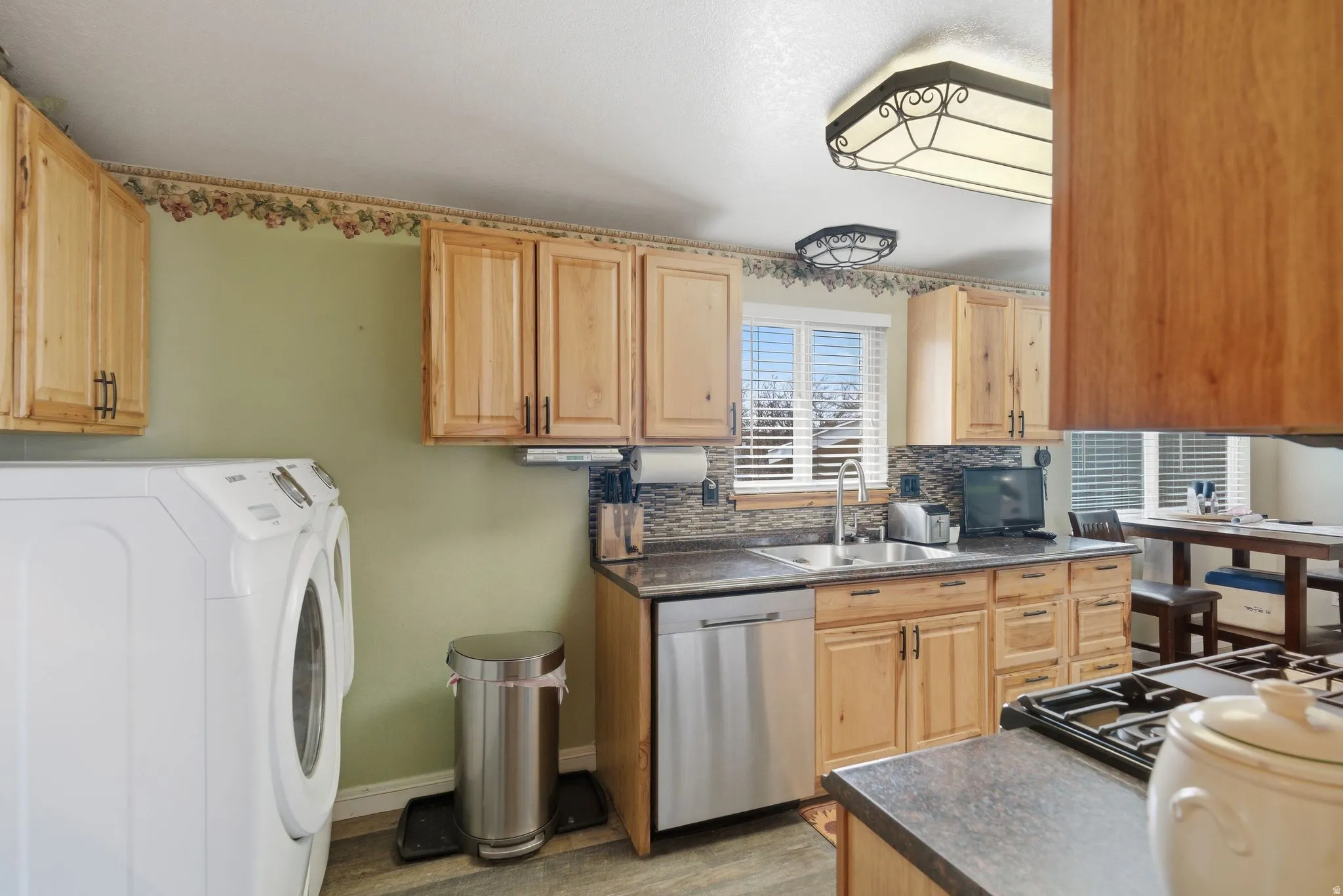 Kitchen featuring dark countertops, decorative backsplash, stainless steel dishwasher, black gas cooktop, and light wood finish cabinets