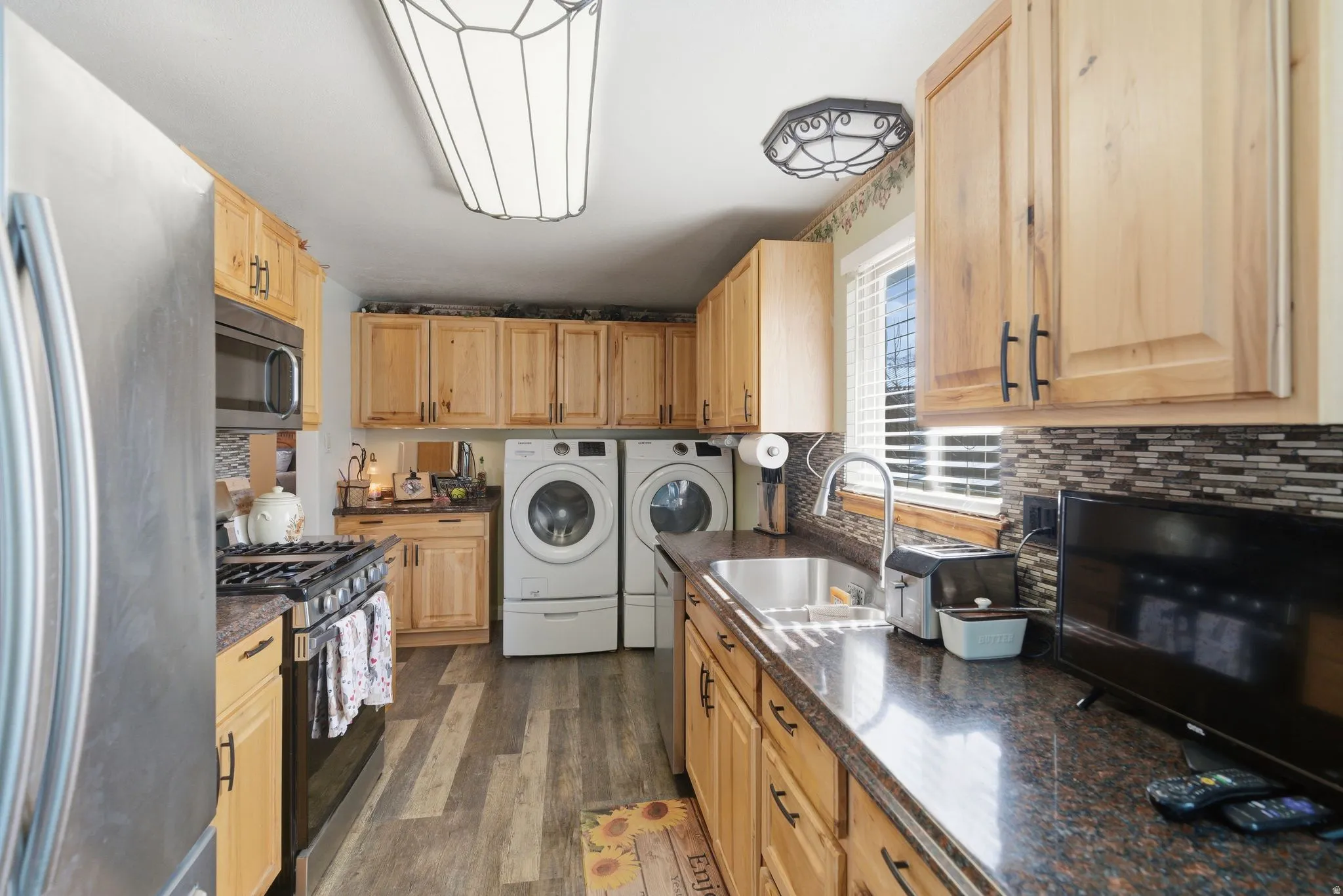 Kitchen featuring stainless steel appliances, light wood finish cabinets, separate washer and dryer, and dark wood finished floors