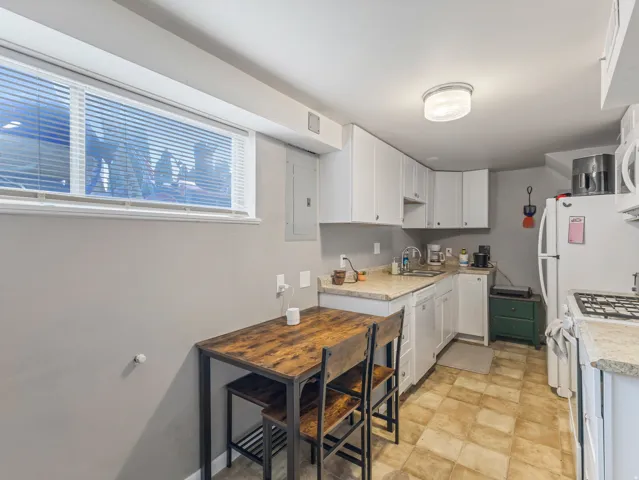 Kitchen with light countertops, white appliances, white cabinetry, and electric panel