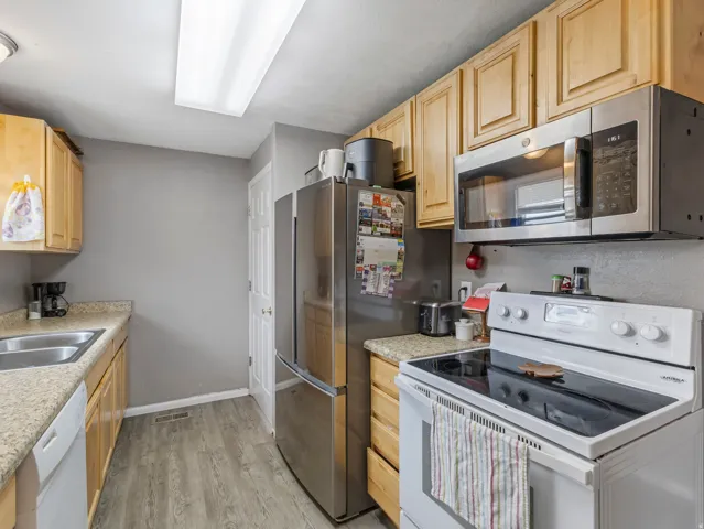 Kitchen with stainless steel appliances, light wood finish cabinetry, light wood-style floors, and light stone countertops