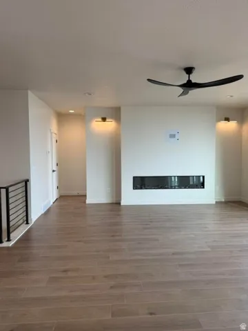 Unfurnished living room featuring wood finished floors, ceiling fan, a glass covered fireplace, and recessed lighting