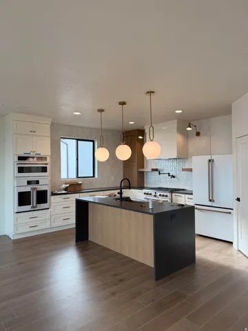 Kitchen featuring premium appliances, a kitchen island with sink, decorative backsplash, hanging light fixtures, and dark stone counters