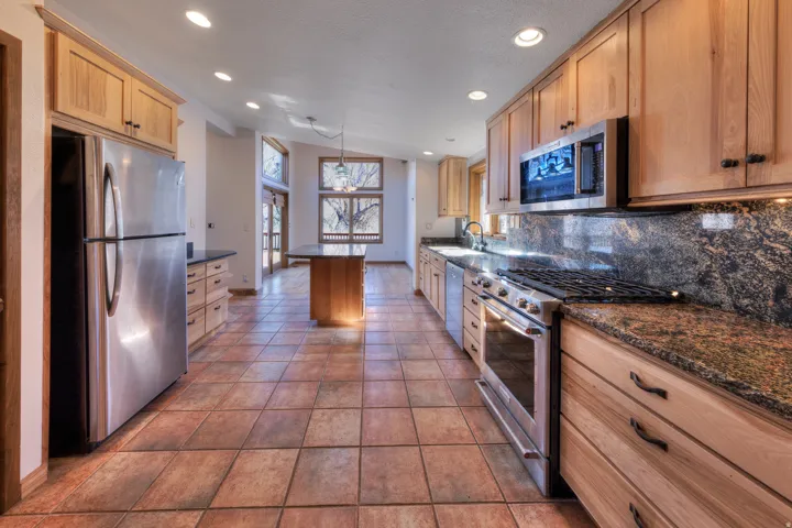 Kitchen featuring stainless steel appliances, granite countertops, a kitchen island, Saltillo tile flooring, and granite backsplash.