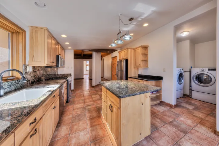 Kitchen with light wood finish cabinets, open shelves, separate washer and dryer, stainless steel appliances, and a center island