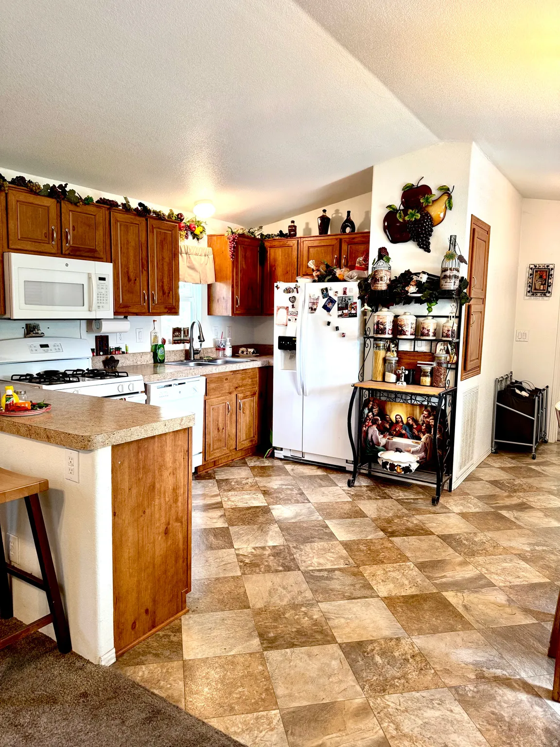Kitchen featuring wood finish cabinetry, white appliances, light countertops, a kitchen breakfast bar, and stone finish flooring