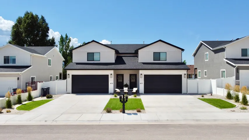 Modern duplex exterior featuring contrasting light and dark siding, a dark asphalt shingle roof, attached garages with dark doors, and a concrete driveway
