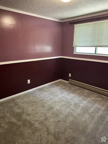 Textured ceiling, wall-mounted light fixture, carpeted flooring, window with blinds, and white trim