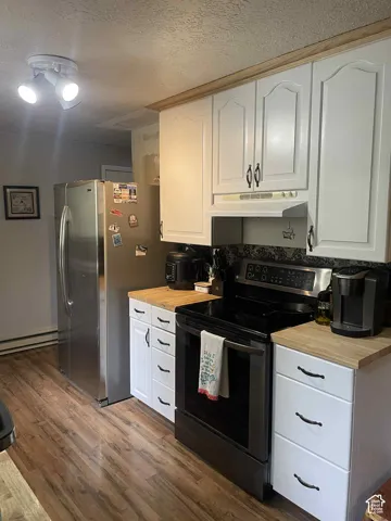 Kitchen with electric range oven, white cabinets, a baseboard heating unit, dark wood-style floors, and a textured ceiling