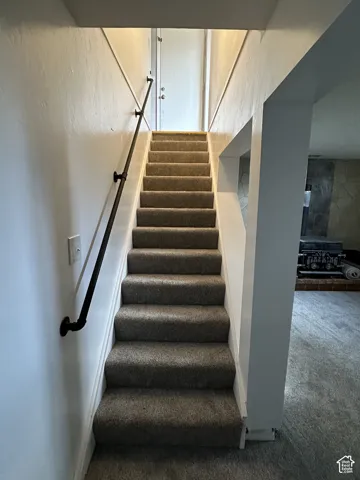 Carpeted staircase with a black metal handrail, white painted walls, and a stone-clad wall in the adjacent lower level