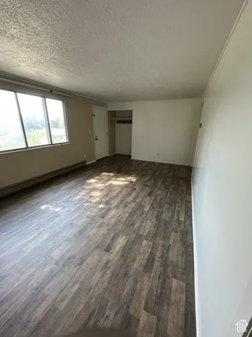 Spacious room featuring wood-finish flooring, a large window, a built-in closet with a hanging rod, and light-toned walls