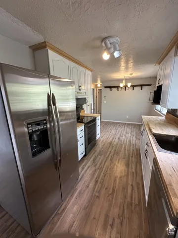 Kitchen featuring stainless steel appliances, white cabinetry with wood trim, wood-finish flooring, and butcher block countertops