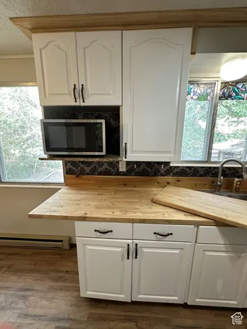 White cabinetry with dark hardware, wood-finish countertops, decorative backsplash, and wood-finish flooring