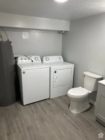 Dedicated laundry room featuring side-by-side GE washer and dryer units, wood-finish flooring, ample counter space along the upper wall, and a full bathroom with white porcelain toilet and vanity cabinetry