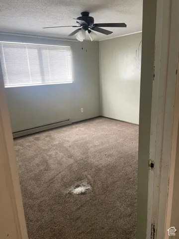 Bedroom 2, Empty room featuring a textured ceiling, a ceiling fan, light carpet, and baseboard heating