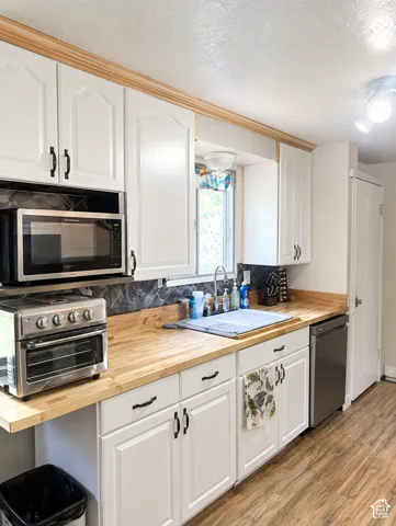 White shaker-style cabinetry with black hardware, wood-finish countertops, geometric tile backsplash, and wood-look flooring