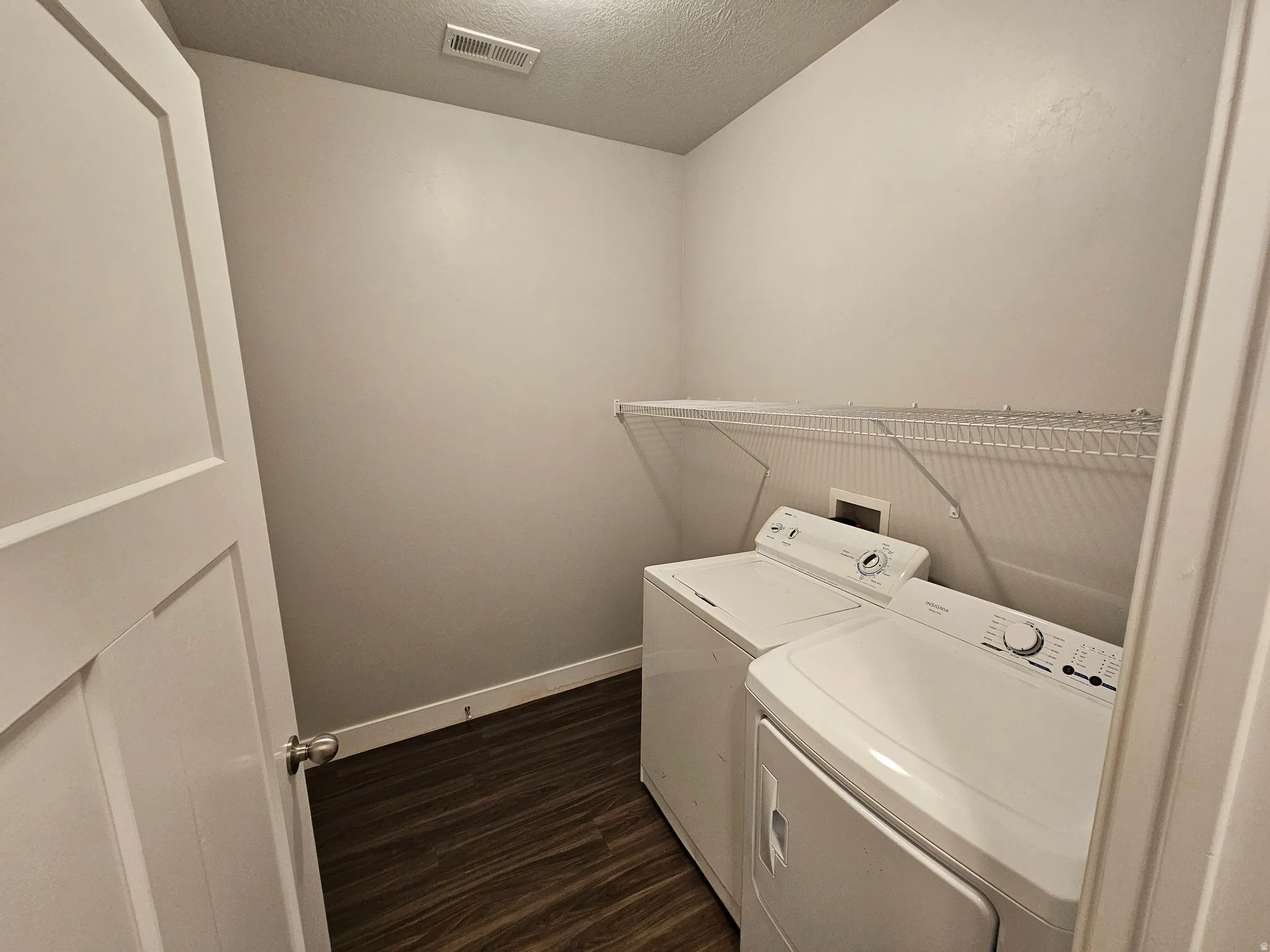 Laundry room with dark wood-type flooring, a textured ceiling, and washer and clothes dryer