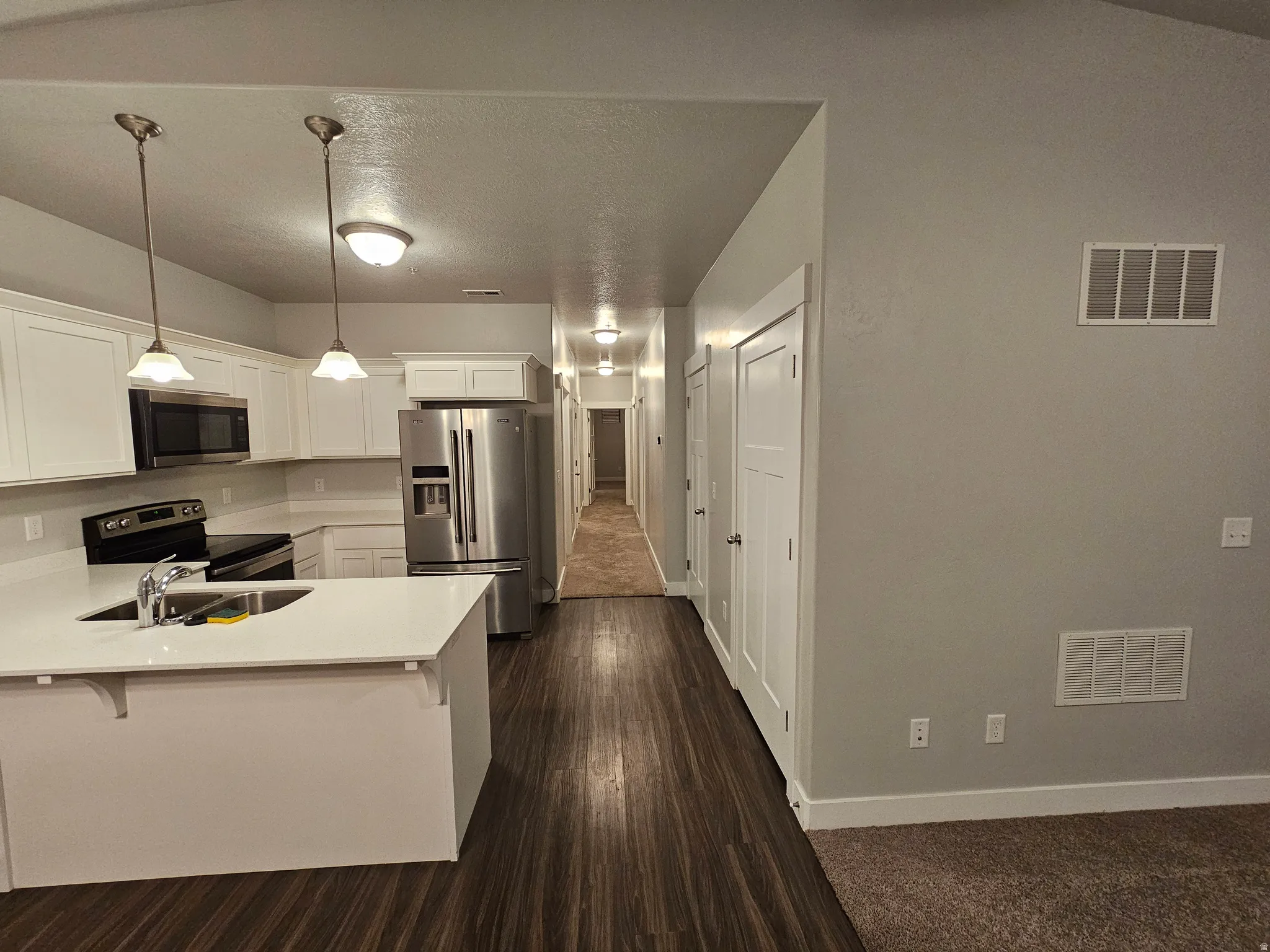 Kitchen featuring white cabinetry, stainless steel appliances, a peninsula, a breakfast bar, and pendant lighting