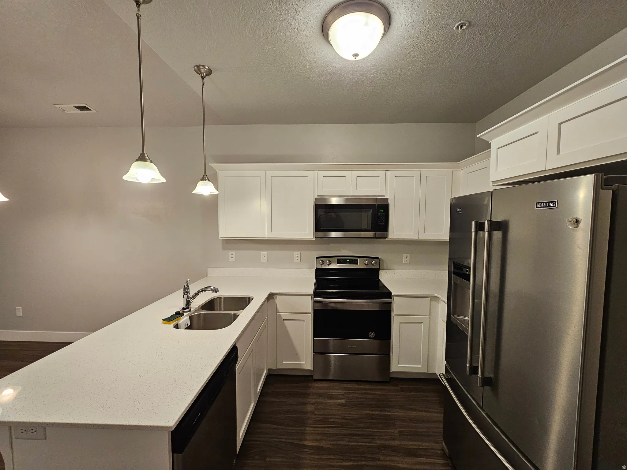 Kitchen with stainless steel appliances, white cabinets, dark wood-style floors, and a textured ceiling