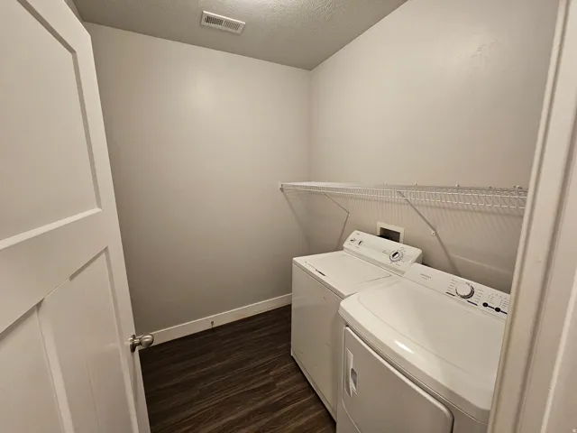 Laundry room with dark wood-type flooring, a textured ceiling, and washer and clothes dryer