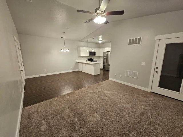 Unfurnished living room featuring hanging lights, ceiling fan, dark colored carpet, and vaulted ceiling