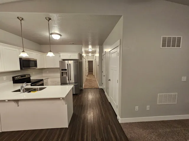 Kitchen featuring white cabinetry, stainless steel appliances, a peninsula, a breakfast bar, and pendant lighting