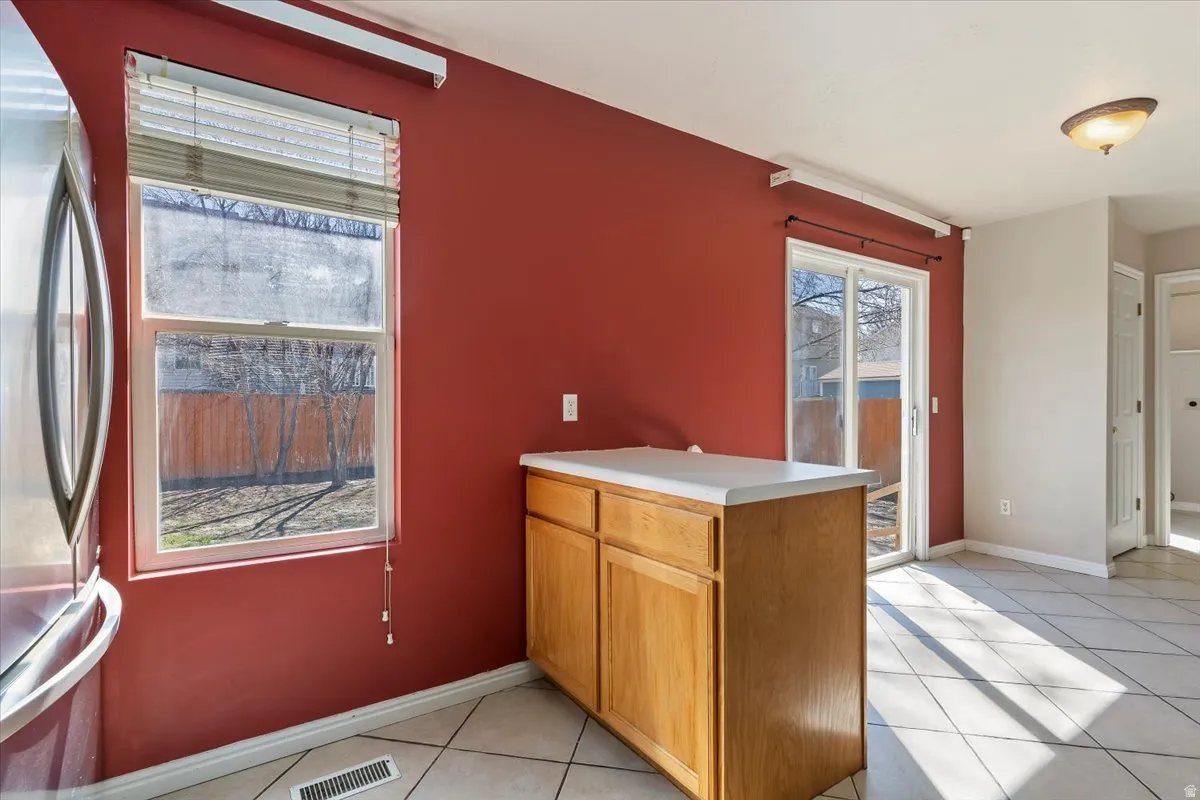 Kitchen with a peninsula, light countertops, freestanding refrigerator, wood finish cabinets, and light tile patterned floors