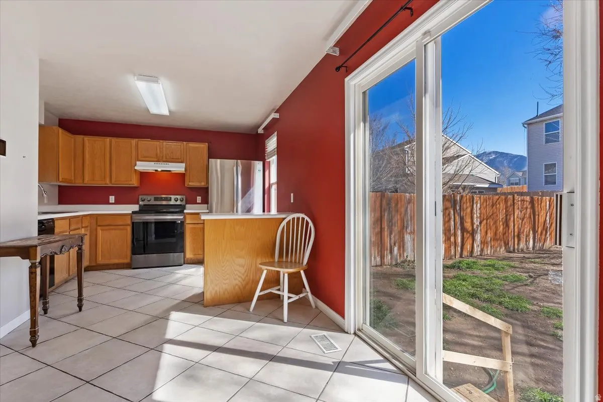 Kitchen with light countertops, stainless steel appliances, wood finish cabinetry, light tile patterned flooring, and a peninsula